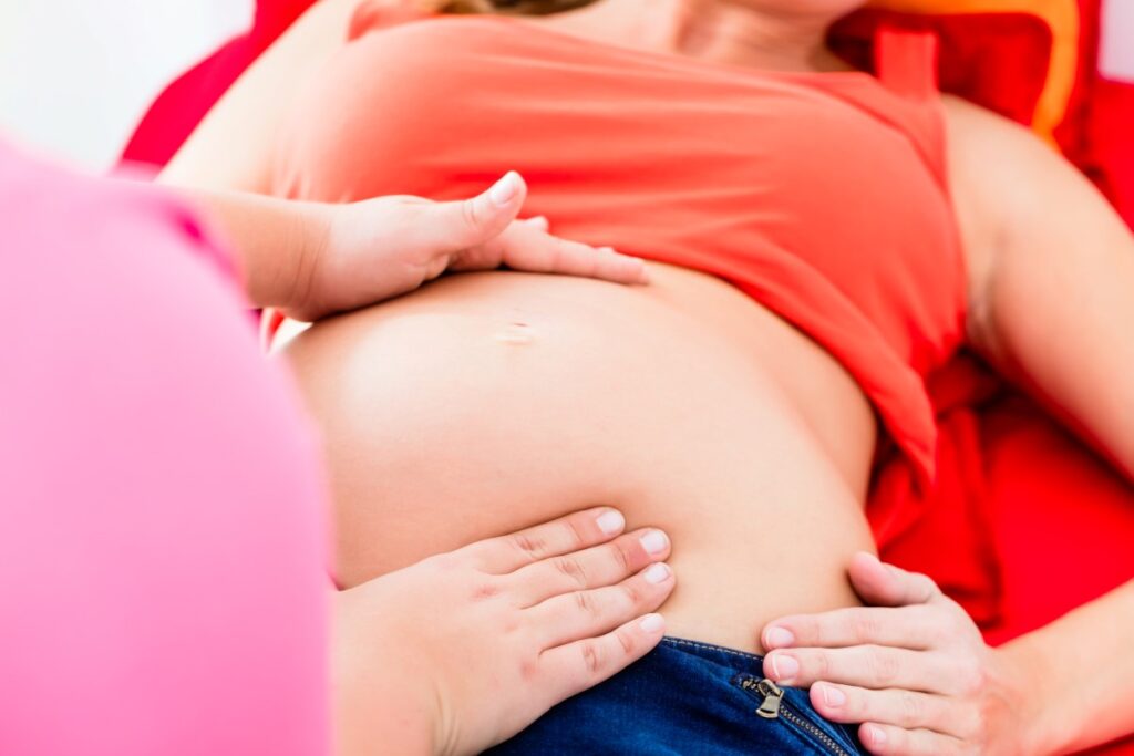 Close-up van iemand die met beide handen bij een zwangere vrouw de positie van de baby bepaalt.